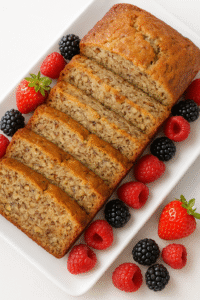 picture of finished, sliced and plated banana bread on a white platter with blackberries, raspberries and strawberries lining th esides of the sliced bread.